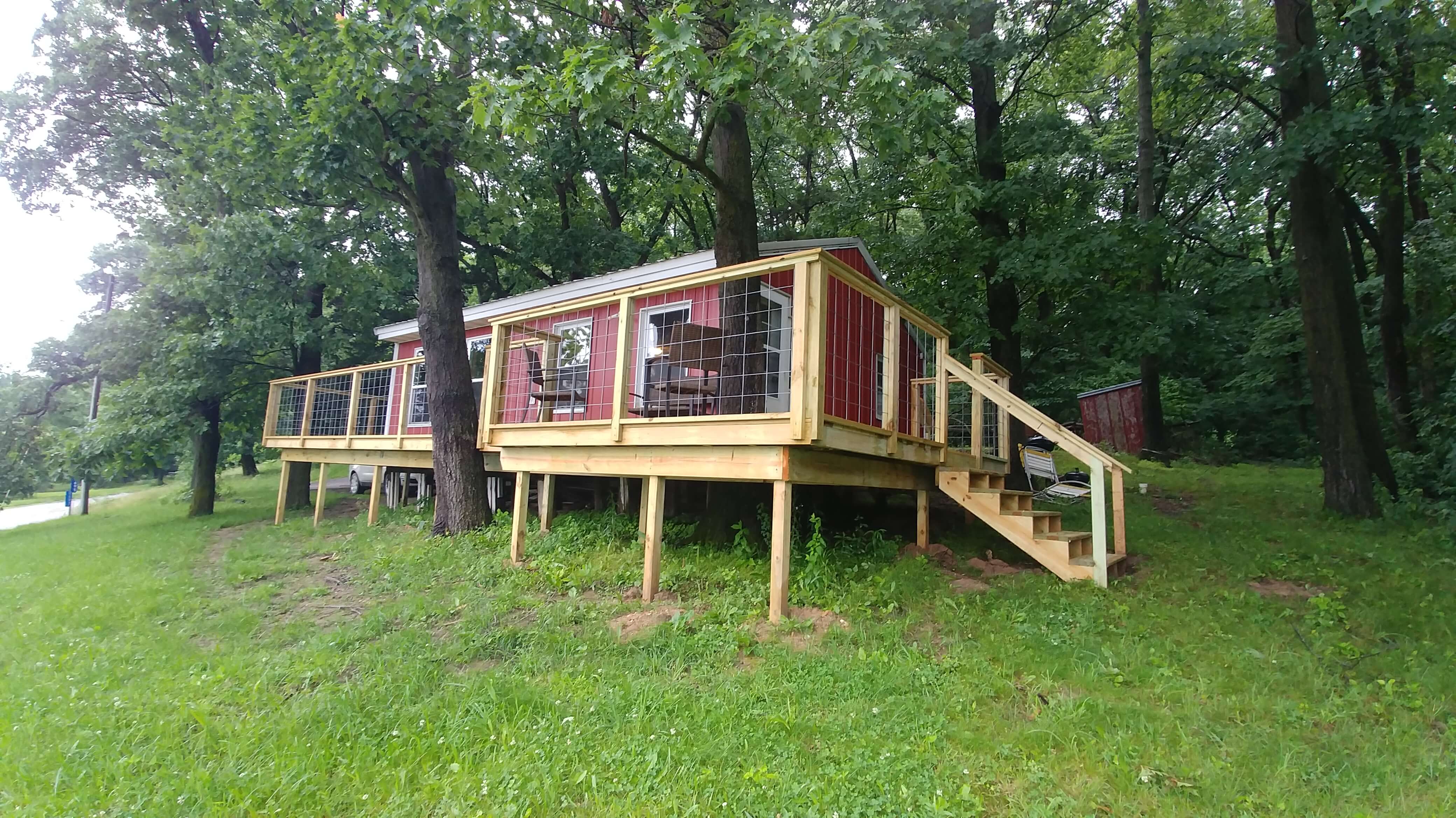 Red cabin with large deck on hill with trees surrounding.